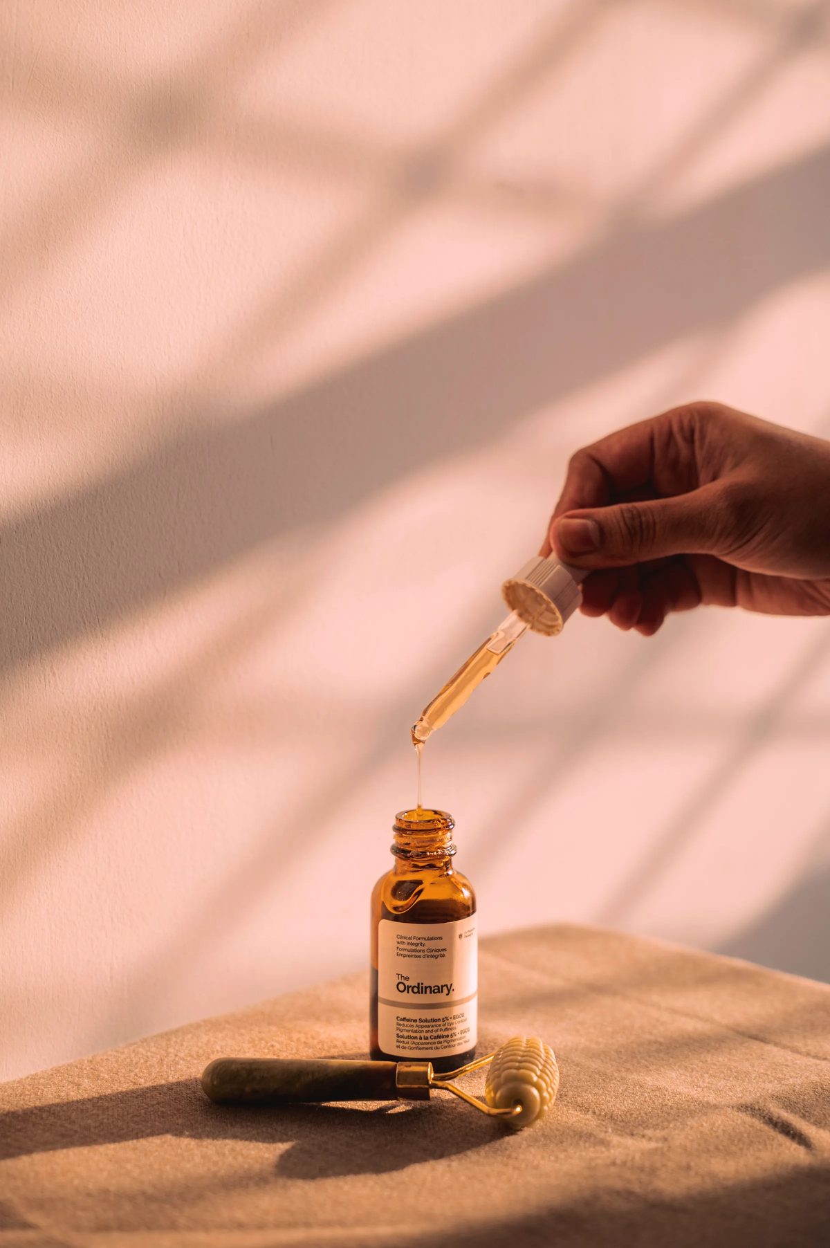 A dropper held over an amber serum bottle in warm light